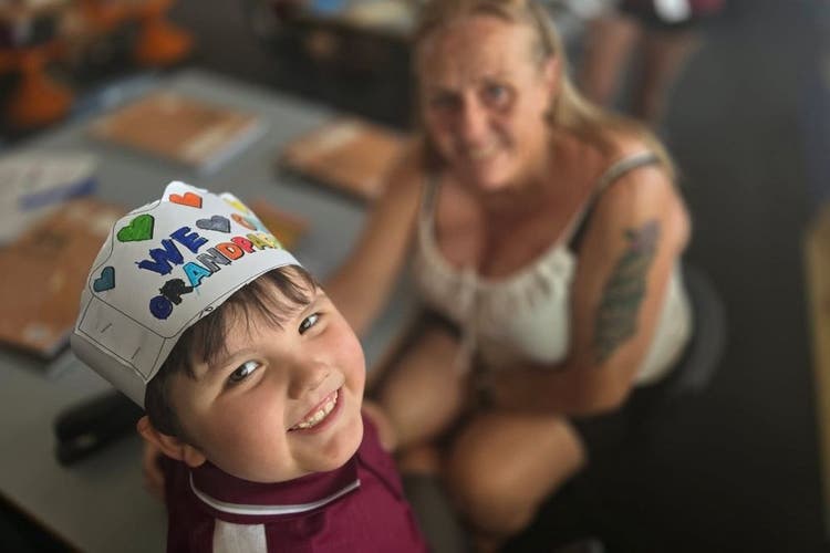 A boy looks up at the camera smiling and wearing a cardboard hat that says
