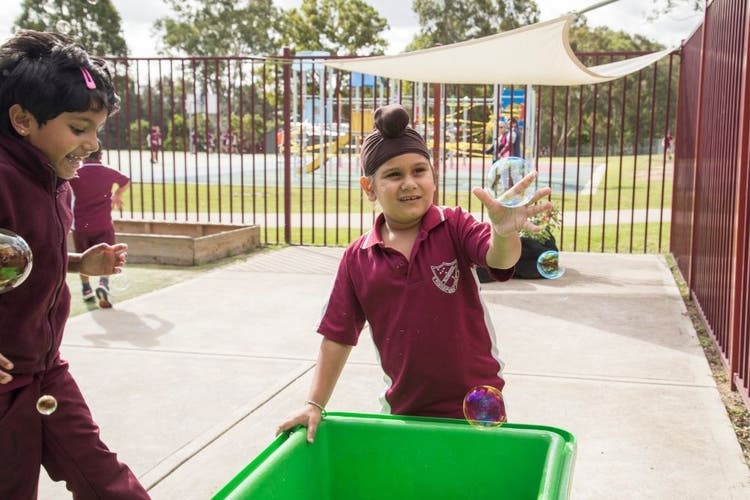 A child stands in front of a waterplay tray and is reaching out for a bubble which is floating through the air.
