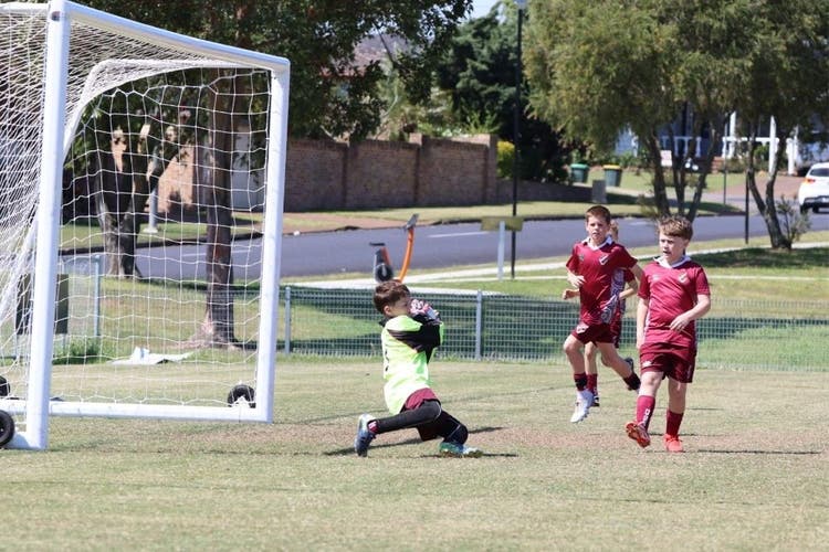 A goal keeper in a yellow top catches a ball as two other players run over.