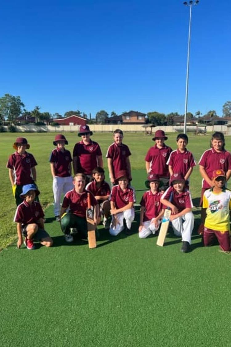 A group of cricket player stand or squat together with 2 plays holding cricket bats.