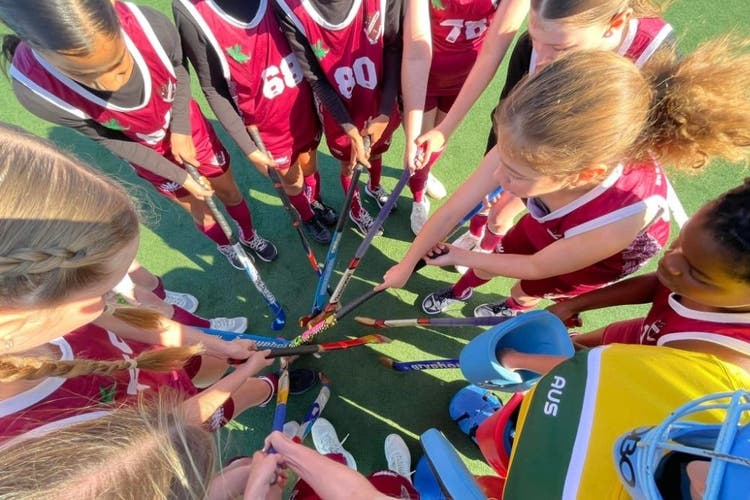 The photo looks down on the heads of a group of students standing in a circle with hockey sticks in the centre of the photo.