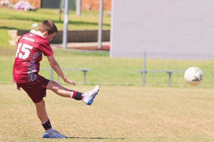 A boy kicks a soccer ball. His left leg is in the air and the soccer ball flies through the air on the right of the photo.