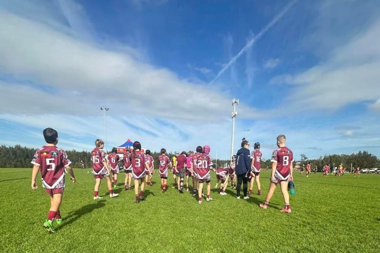 A group of rugby leage players have their backs to the camera as they walk back onto the field with a bight blue sky above them.